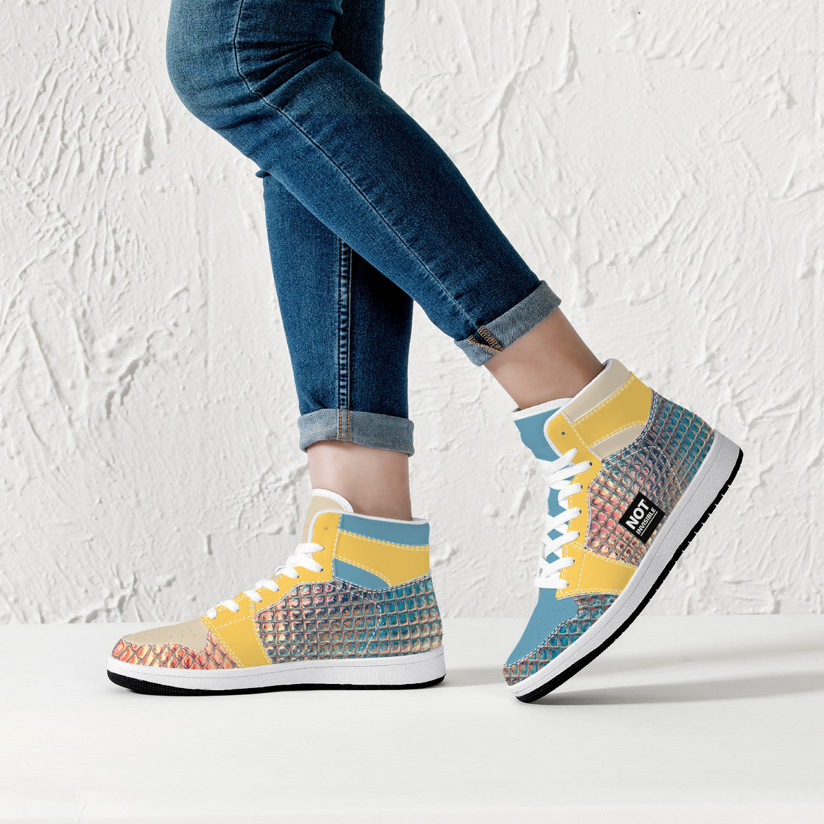Colorful high-top sneakers worn with blue jeans against a white textured wall.