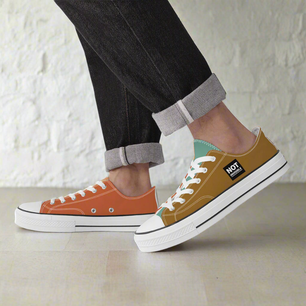 Two pairs of sneakers, one orange and one brown, worn by a person with rolled-up jeans.